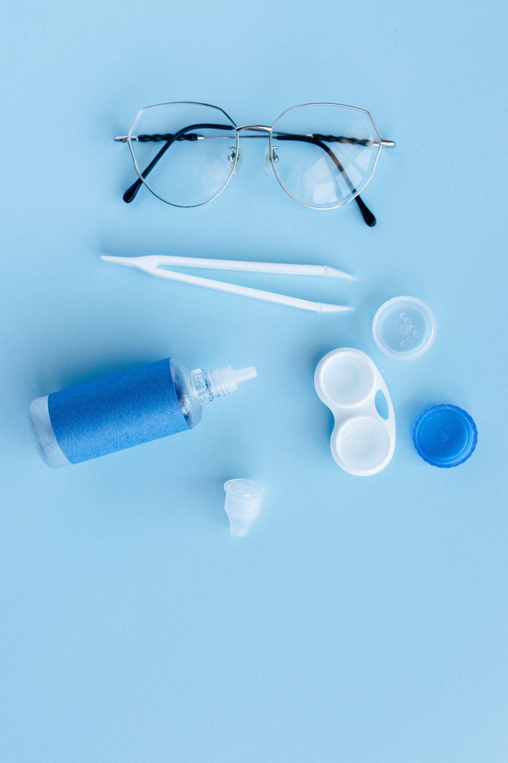 Flat lay of eye care essentials including glasses and contact lens solution on a blue background.